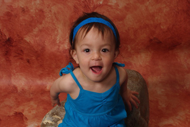 Julia climbs on a rock during her portrait session with bright orange background contrasts nicely against her bright blue summer strappy dress with matching sandals and headband