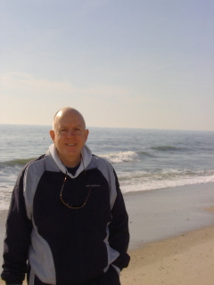 Kevin smiling standing on the beach with the waves rolling in behind him.